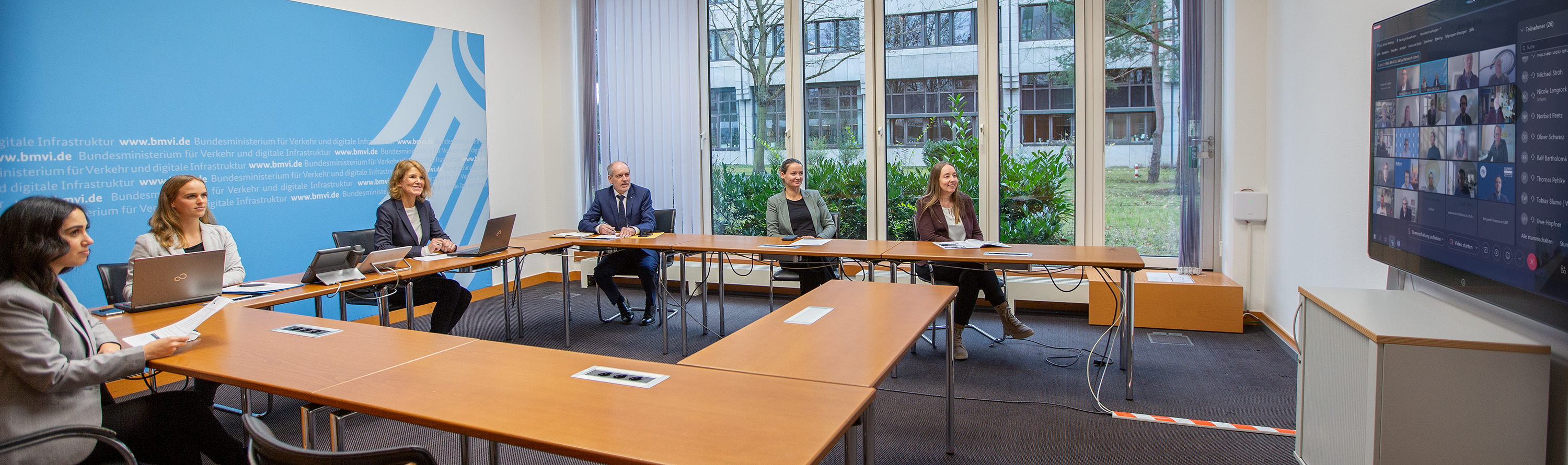 Beteiligte von PIANC Deutschland sitzen an einem Tisch mit Blick auf einen Monitor mit zugeschalteten Personen.
